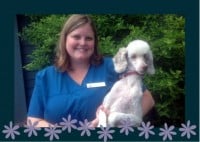 A woman in blue scrubs is smiling and holding a small white poodle outside, with green bushes in the background and a floral border at the bottom of the image.